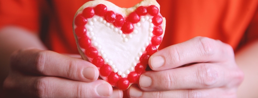 misshapen heart sugar cookie in a man's hands to illustrate the meaning behind valentine's day