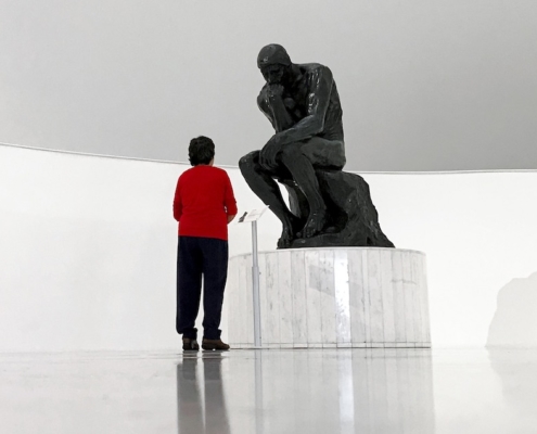 image of man in red shirt standing in front of The Thinker to illustrate that thinking burns calories