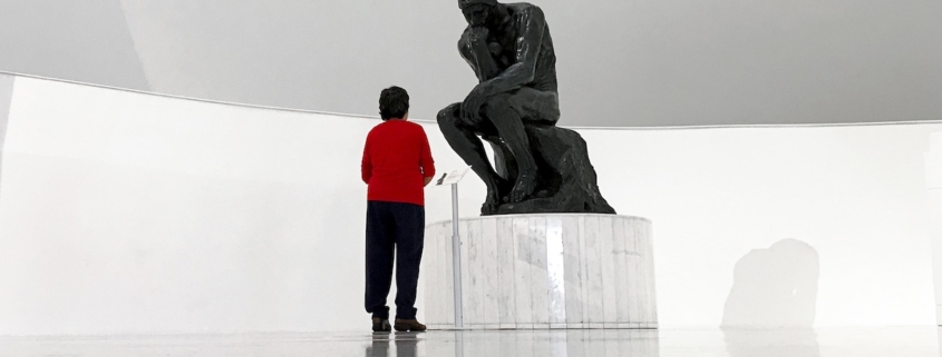 image of man in red shirt standing in front of The Thinker to illustrate that thinking burns calories