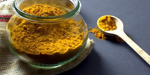 a glass jar of powdered turmeric with a spoon to illustrate the sex benefits of turmeric