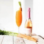 Easter Cocktail in a champagne flute with a bottle of sparkling wine behind it and carrots laying on the table