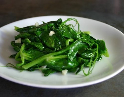 closeup of garlicky pea tendrils on a white plate