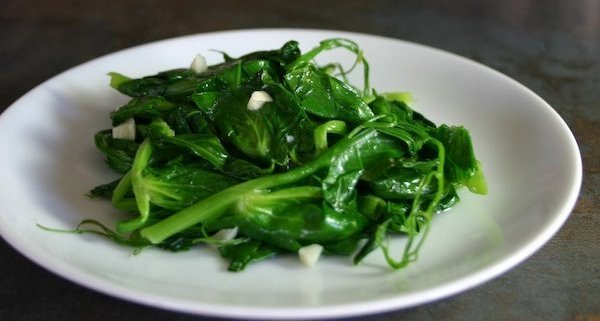 closeup of garlicky pea tendrils on a white plate