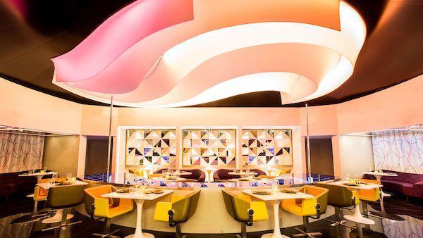 The dining room of She restaurant Cancun with pink lights and rows of white tables for two