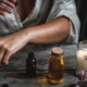 dark-skinned woman applying castor oil to her arm with a bottle of oil and a candle in the foreground to illustrate castor oil benefits to skin