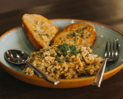 wild and brown rice pilaf in a clay bowl with a fork and spoon and toasted French bread