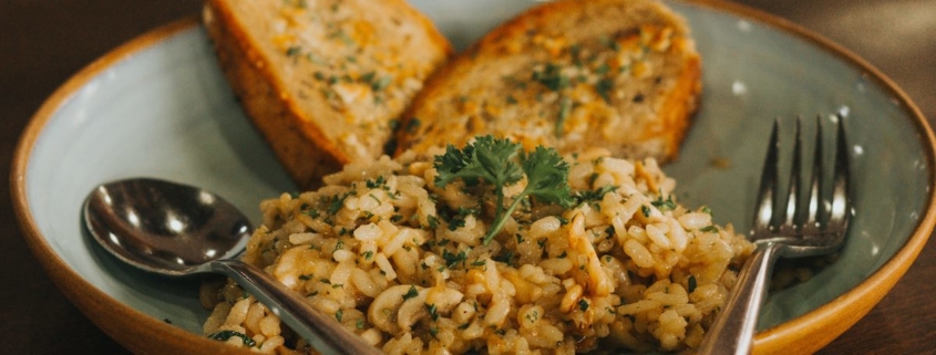 wild and brown rice pilaf in a clay bowl with a fork and spoon and toasted French bread