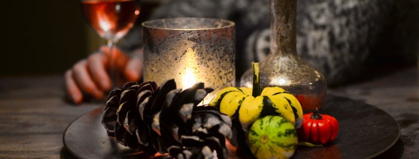 pinecone and candle still life in foreground with woman in a grey sweater drinking rosé in the background to illustrate our wine pairing with turkey article for Thanksgiving