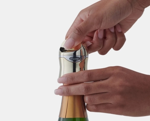 a pair of hands putting a gold metallic rabbit champagne stopper on a bottle of sparkling wine