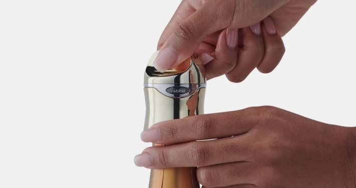 a pair of hands putting a gold metallic rabbit champagne stopper on a bottle of sparkling wine