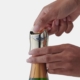 a pair of hands putting a gold metallic rabbit champagne stopper on a bottle of sparkling wine