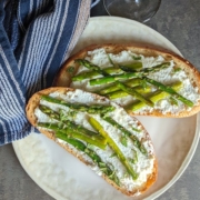 Ricotta Toast Recipe with Asparagus, Lemon and Mint 2 overhead shot of ricotta toast with asparagus on a cream colored plate with a blue napkin