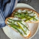 overhead shot of ricotta toast with asparagus on a cream colored plate with a blue napkin
