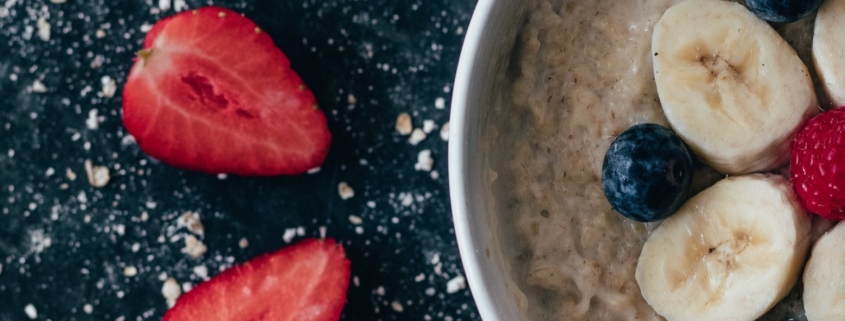 overnight steel cut oats in a white bowl with bananas and blueberries on top and strawberry slices on the side