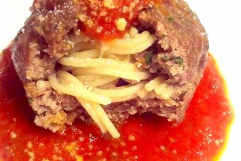 closeup of giant meatball stuffed with spaghetti in marinara sauce on a white plate