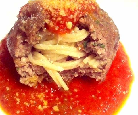 closeup of giant meatball stuffed with spaghetti in marinara sauce on a white plate
