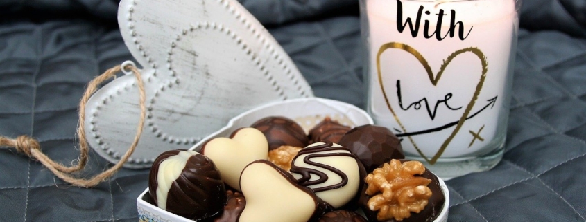 chocolate aphrodisiac image of chocolates in a white, heart-shaped box with a candle flickering in the background