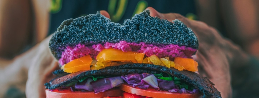 a pair of hands holding a colorful vegan sandwich