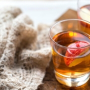 closeup of hot apple cider cocktail next to a knit beige blanket on a wooden table