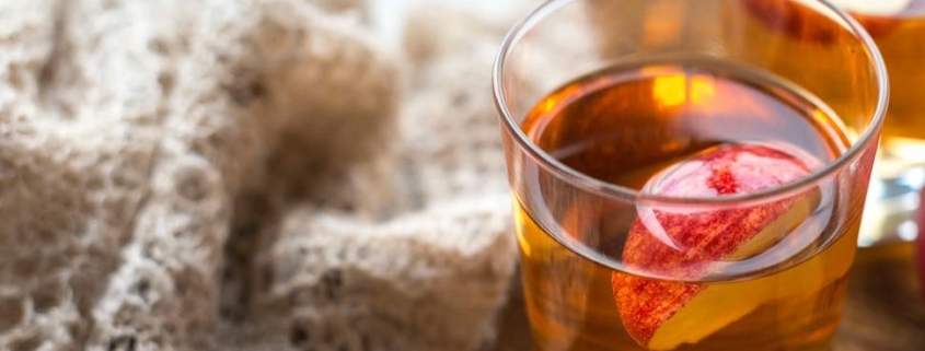 closeup of hot apple cider cocktail next to a knit beige blanket on a wooden table