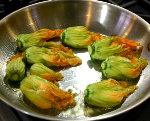 closeup of stuffed courgette flowers being cooked in a sauté pan