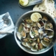 Closeup of steamed clams in a metal pot on a dark blue background