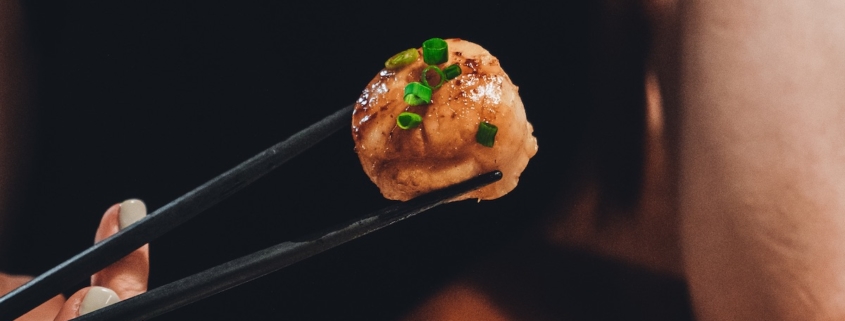 woman's hand holding a scallop with chopsticks