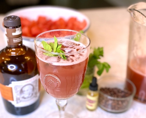 The Best Watermelon Cocktail Recipe 2 Watermelon cocktail next to a bottle of rum with a bowl of watermelon behind it and a pitcher of the rum punch on the side
