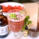 Watermelon cocktail next to a bottle of rum with a bowl of watermelon behind it and a pitcher of the rum punch on the side