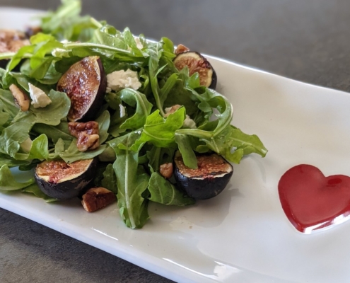 grilled fig and arugula salad on a white plate with a red heart