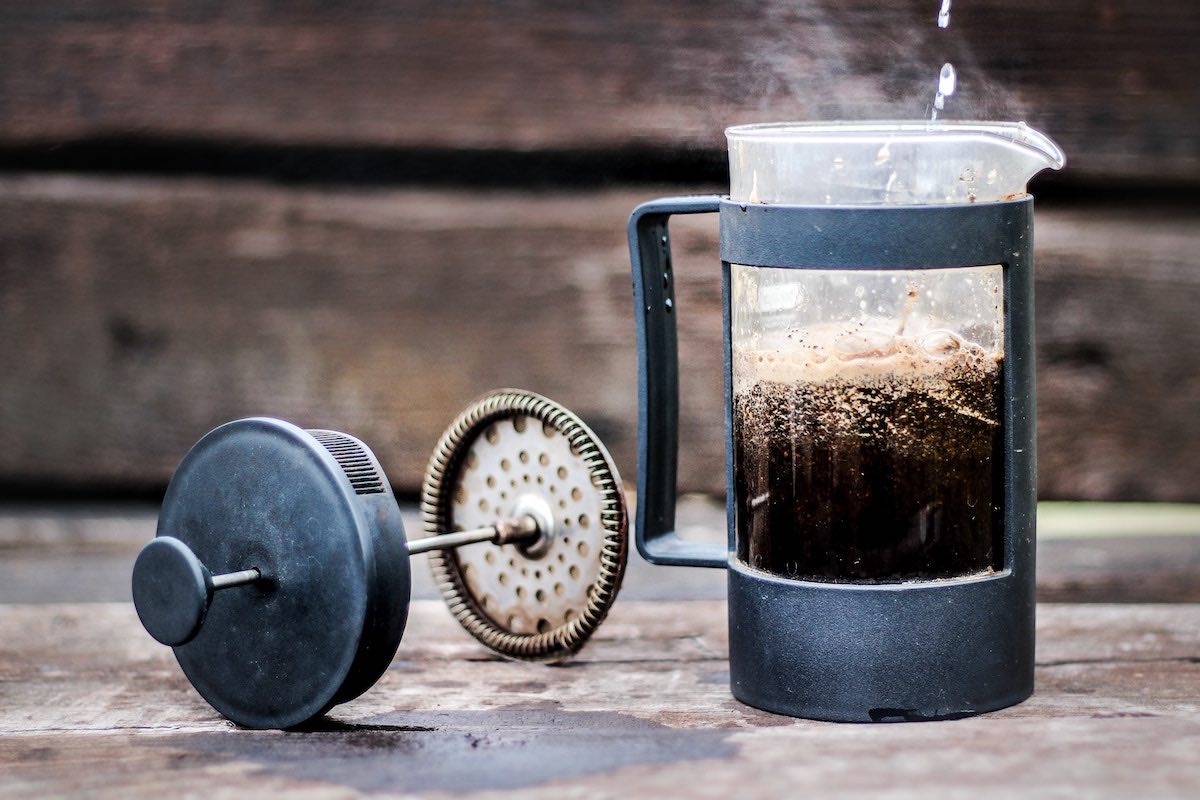 A french press coffee maker half filled with coffee with the lid sitting beside it