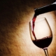 neck of a wine bottle with wine being poured into a stemmed glass on a spotlit, beige background