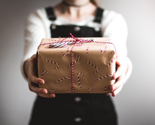 woman in blue overalls giving a butcher paper-wrapped gift to the camera to illustrate our 2021 gift guide