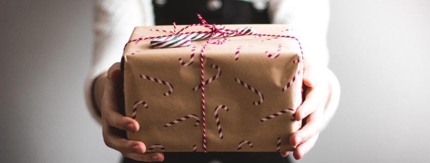 woman in blue overalls giving a butcher paper-wrapped gift to the camera to illustrate our 2021 gift guide