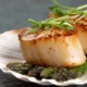 a scallop shell holding two seared scallops on a bed of pesto, topped with sprouts