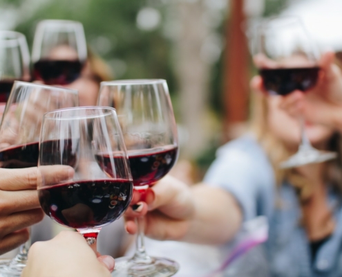 Closeup on the hands of several women toasting with glasses of red wine