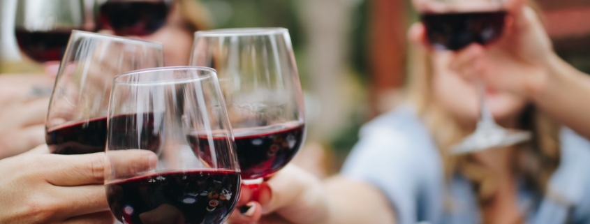 Closeup on the hands of several women toasting with glasses of red wine