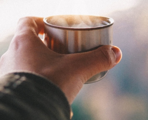 man's hand holding a copper cup of tea at sunrise