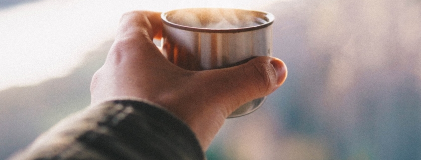 man's hand holding a copper cup of tea at sunrise