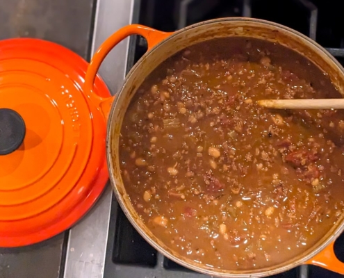 closeup of chili with chocolate in an orange enamel pot on a black stovetop