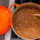 closeup of chili with chocolate in an orange enamel pot on a black stovetop