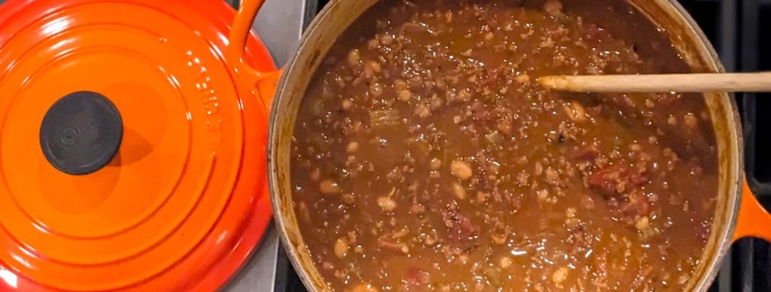 closeup of chili with chocolate in an orange enamel pot on a black stovetop