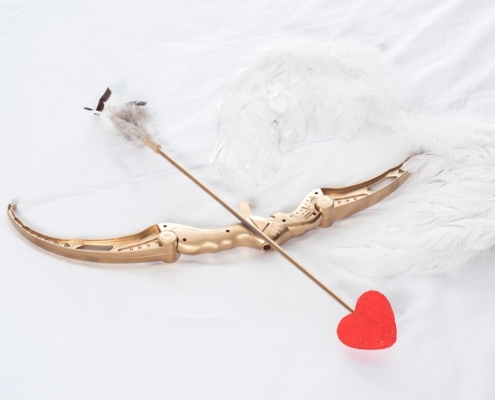 golden bow shooting a red heart arrow on top of white feather wings