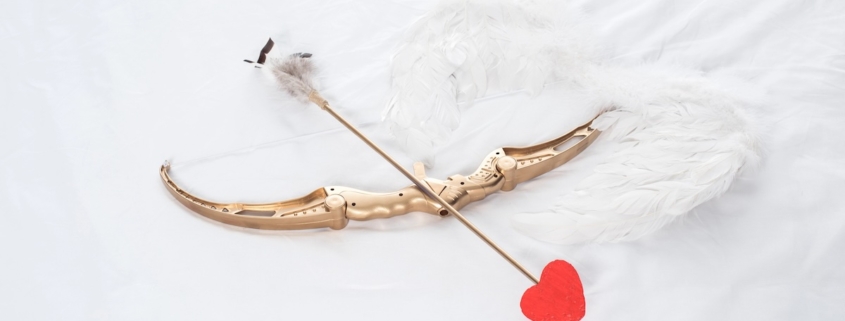golden bow shooting a red heart arrow on top of white feather wings