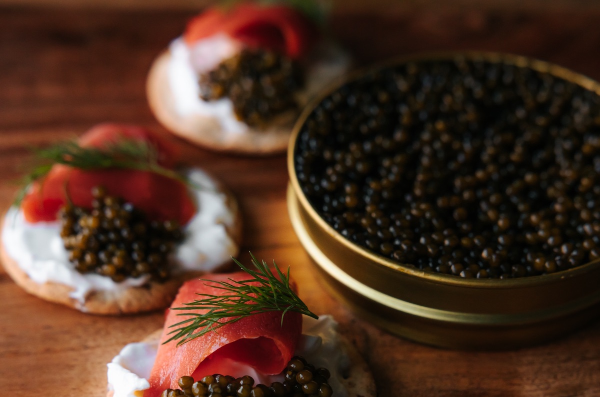 closeup of an open tin of caviar with some canapes on a brown wood table