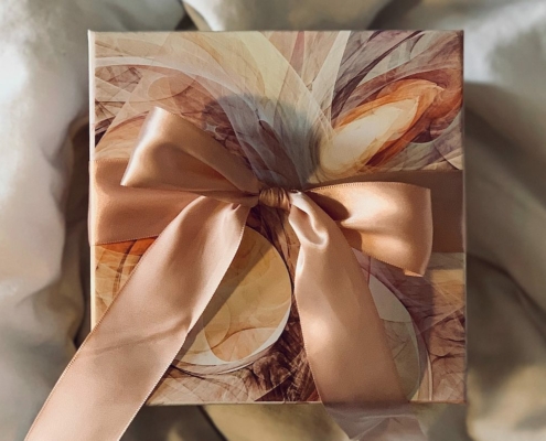 Fancy wrapped present with a large peach bow laying on a fluffy beige comforter