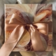Fancy wrapped present with a large peach bow laying on a fluffy beige comforter