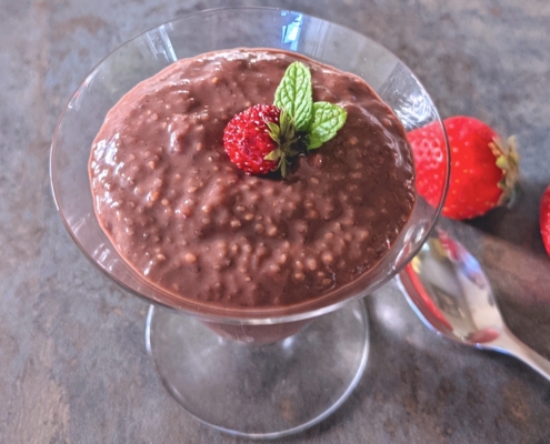 closeup of strawberry chia pudding in a parfait glass with a spoon and fresh strawberries on the side