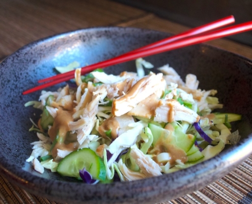 closeup of Asian chicken rice bowl in black pottery with red chopsticks on a bamboo placemat