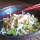 closeup of Asian chicken rice bowl in black pottery with red chopsticks on a bamboo placemat